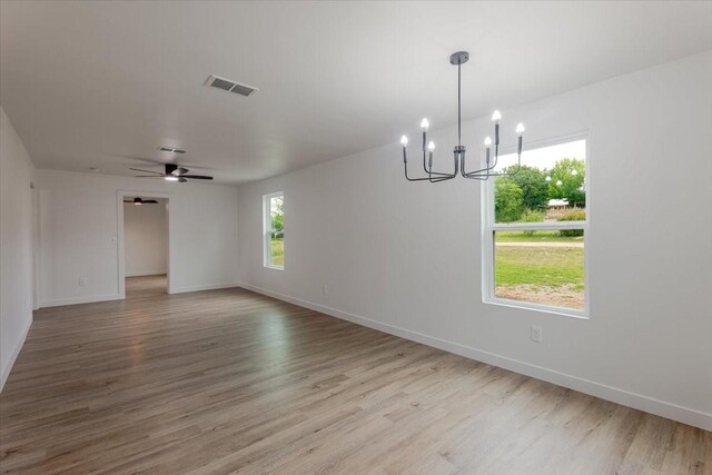 empty room with baseboards, ceiling fan with notable chandelier, wood finished floors, and visible vents