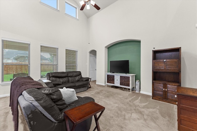 carpeted living area featuring baseboards, a ceiling fan, arched walkways, and a wealth of natural light