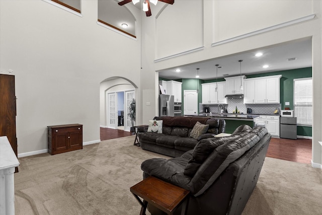 living area with ceiling fan, arched walkways, baseboards, a high ceiling, and light carpet