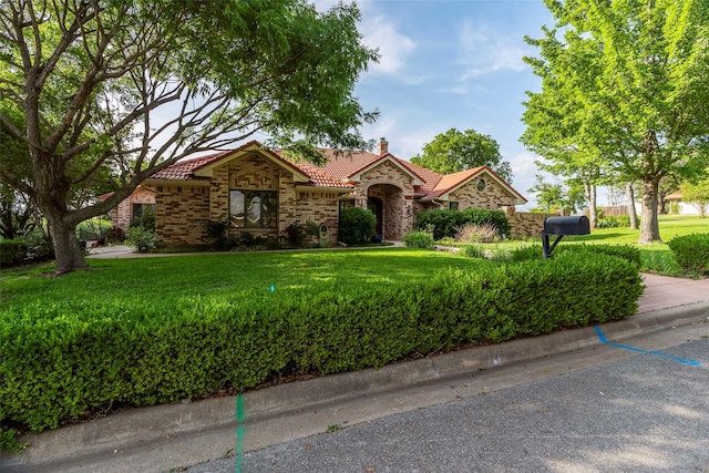 ranch-style house with a tiled roof, stone siding, a chimney, and a front yard