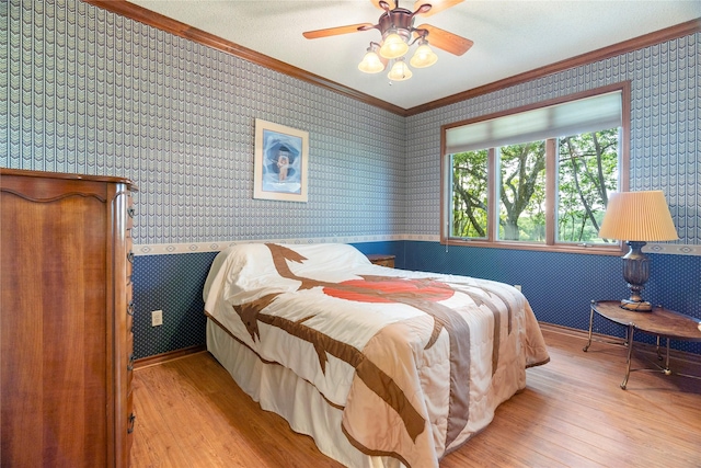 bedroom featuring ornamental molding, a ceiling fan, wallpapered walls, and wood finished floors
