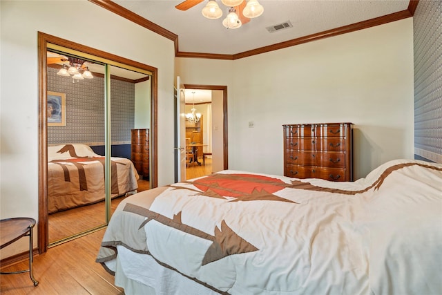 bedroom with visible vents, ornamental molding, a closet, light wood-style flooring, and ceiling fan with notable chandelier