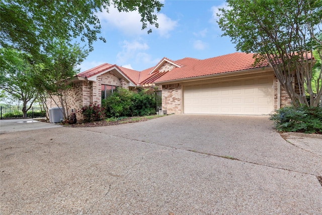 ranch-style home with fence, brick siding, an attached garage, driveway, and a tile roof