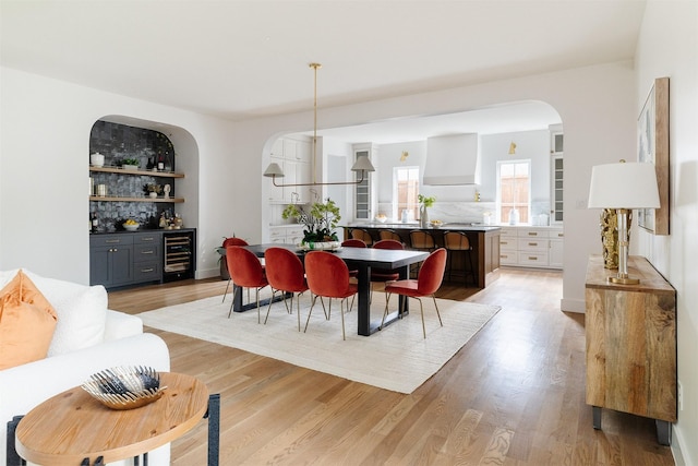dining space with arched walkways, a bar, light wood finished floors, and wine cooler
