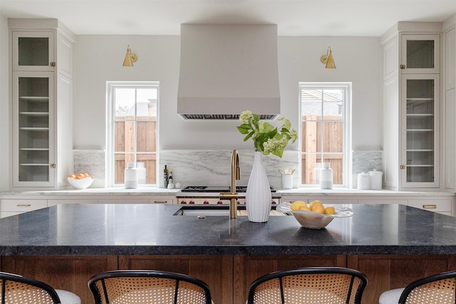 kitchen featuring a kitchen breakfast bar, a wealth of natural light, wall chimney exhaust hood, and dark stone countertops