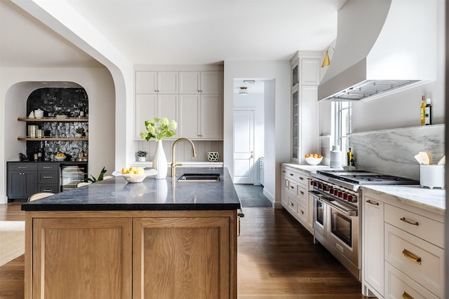 kitchen with dark wood-style floors, extractor fan, dark stone counters, a sink, and double oven range