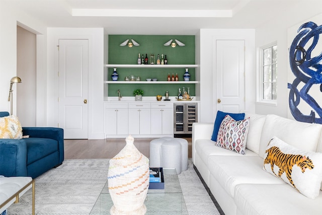 living room with light wood-style floors, a dry bar, a tray ceiling, and beverage cooler