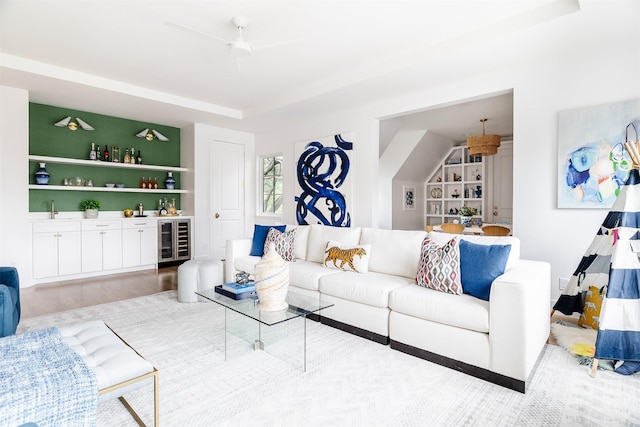 living room with built in features, wood finished floors, beverage cooler, a tray ceiling, and a dry bar