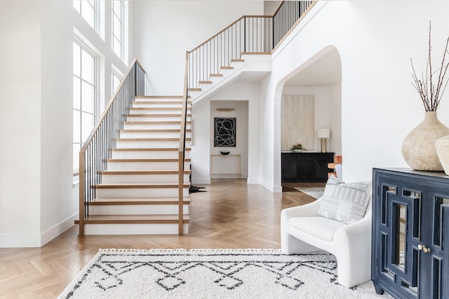foyer entrance featuring baseboards, stairs, a towering ceiling, and arched walkways