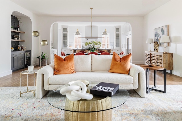 living area with wine cooler, light wood-style floors, baseboards, a bar, and arched walkways
