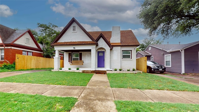 view of front of house with covered porch, brick siding, fence, and a front yard