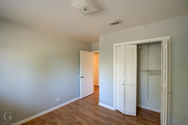 unfurnished bedroom with baseboards, wood finished floors, visible vents, and a closet