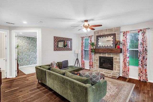 living area with visible vents, wood-type flooring, baseboards, a stone fireplace, and ceiling fan