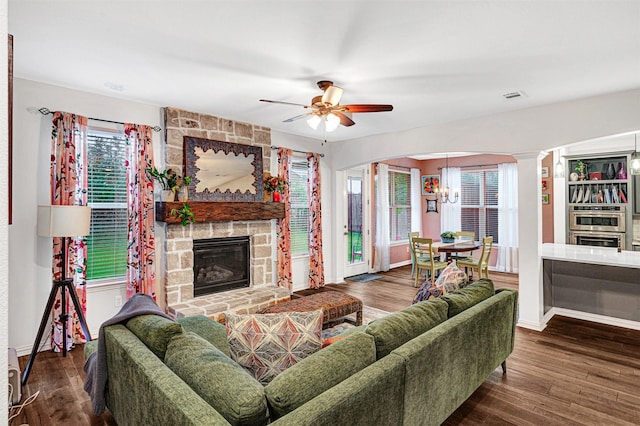 living room with wood finished floors, visible vents, baseboards, and a stone fireplace