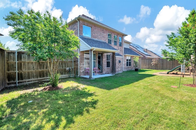 back of property with a patio area, brick siding, a fenced backyard, a lawn, and a playground
