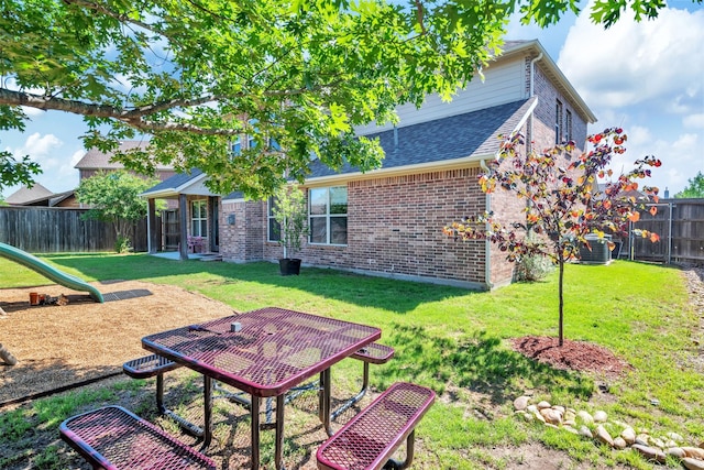 back of property featuring a fenced backyard, roof with shingles, brick siding, and a lawn