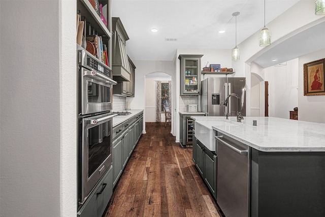 kitchen featuring arched walkways, stainless steel appliances, decorative backsplash, and a sink