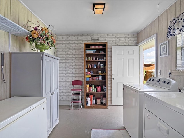 laundry area featuring cabinet space, brick wall, wood walls, and washing machine and dryer