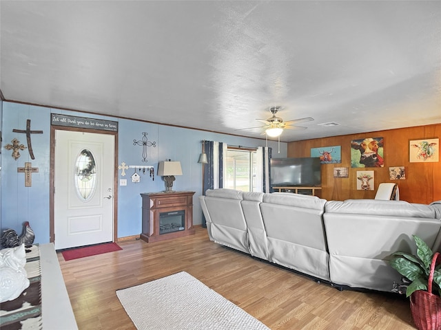 living room with wooden walls, a fireplace, a ceiling fan, and light wood-style flooring