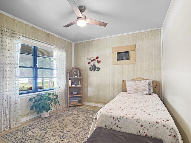 bedroom featuring ceiling fan, wood finished floors, baseboards, wooden walls, and ornamental molding