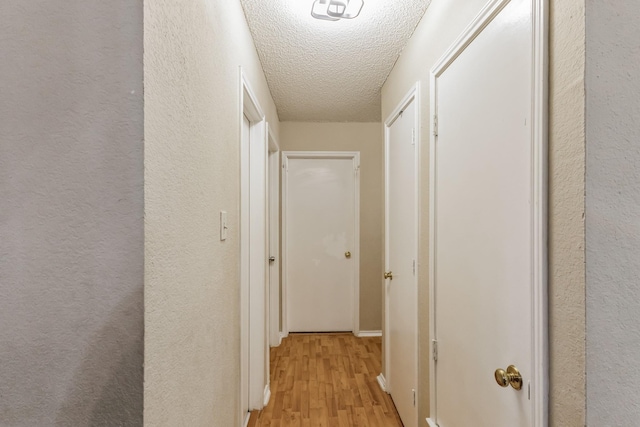 corridor with light wood-style floors, a textured wall, and a textured ceiling