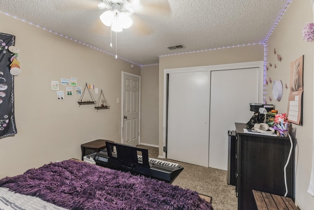 carpeted bedroom with ceiling fan, a closet, a textured ceiling, and visible vents
