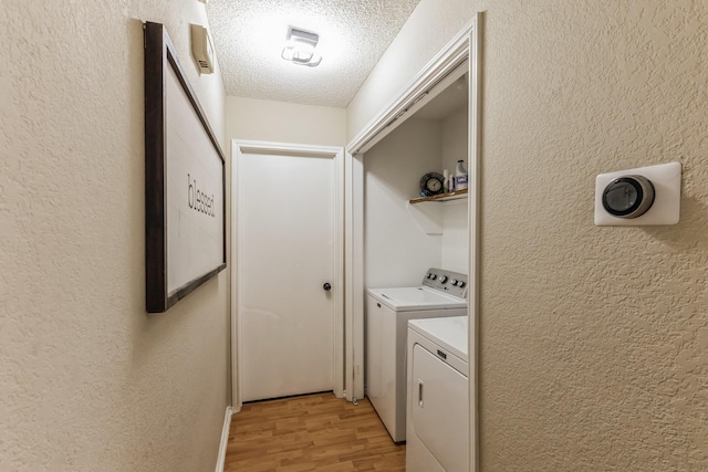 clothes washing area featuring light wood-style floors, a textured wall, a textured ceiling, and washer and dryer