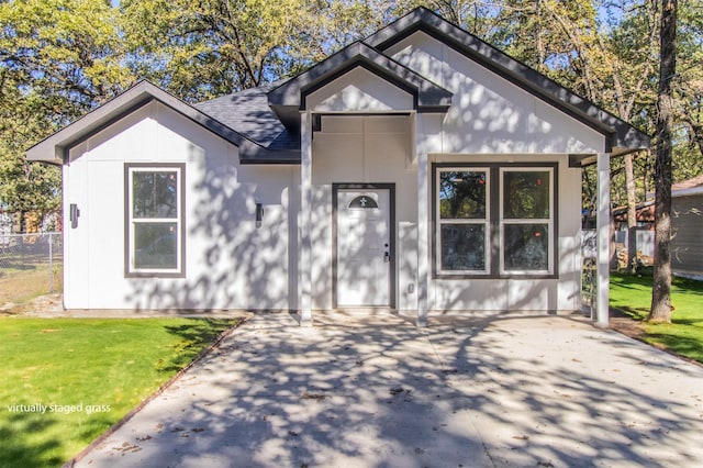 view of front of house featuring roof with shingles, fence, and a front lawn