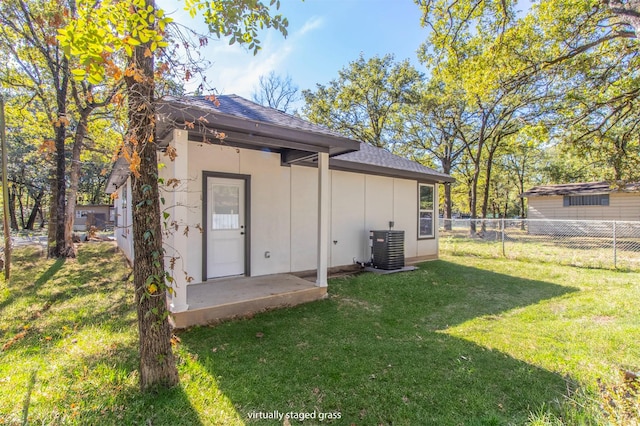 back of property with a lawn, central AC, fence, and roof with shingles