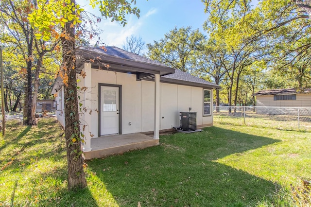 back of house featuring a lawn, a shingled roof, fence, and central AC unit