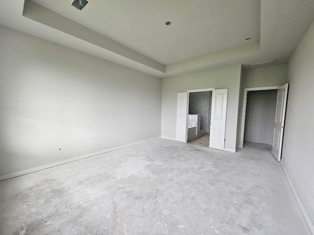 unfurnished bedroom featuring baseboards, connected bathroom, a raised ceiling, and unfinished concrete floors