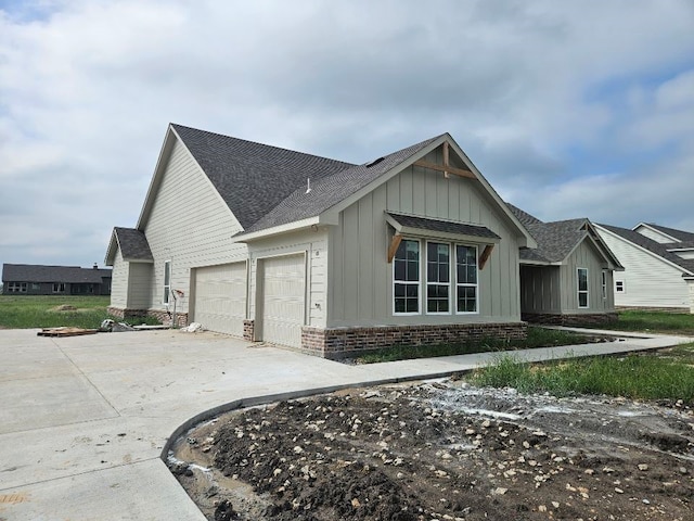 view of home's exterior featuring a shingled roof, an attached garage, brick siding, board and batten siding, and driveway