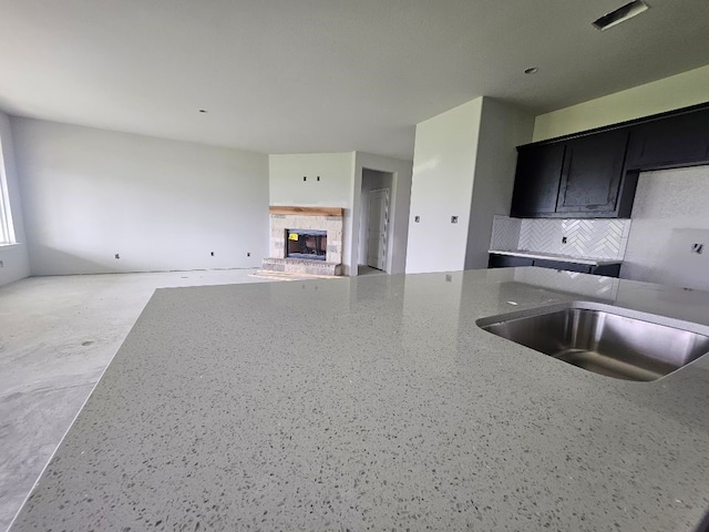 kitchen featuring a sink, dark cabinetry, stone countertops, a tiled fireplace, and tasteful backsplash