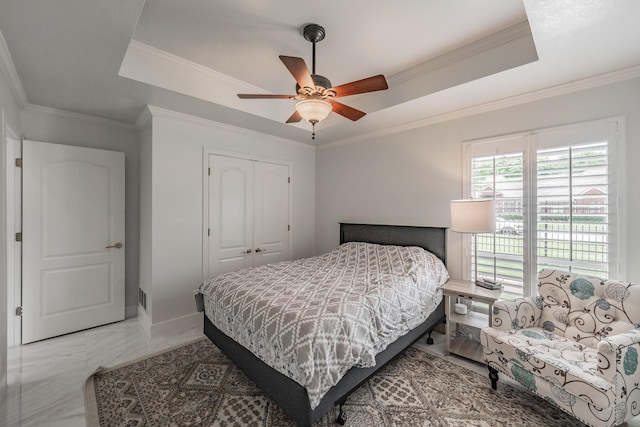 bedroom with a tray ceiling, a closet, ornamental molding, and a ceiling fan
