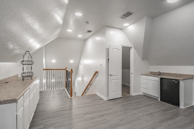 bonus room with light wood-type flooring, lofted ceiling, a sink, a textured ceiling, and baseboards
