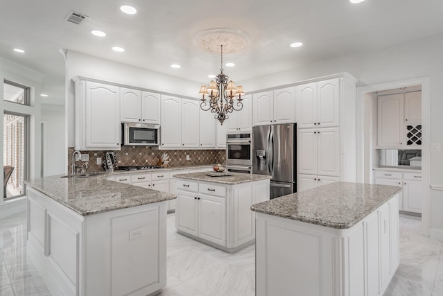 kitchen featuring appliances with stainless steel finishes, a kitchen island, a sink, light marble finish floors, and a chandelier