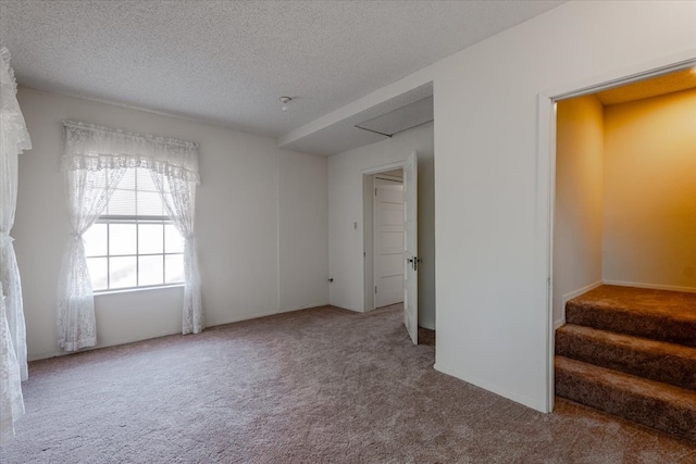 carpeted spare room with a textured ceiling and stairway