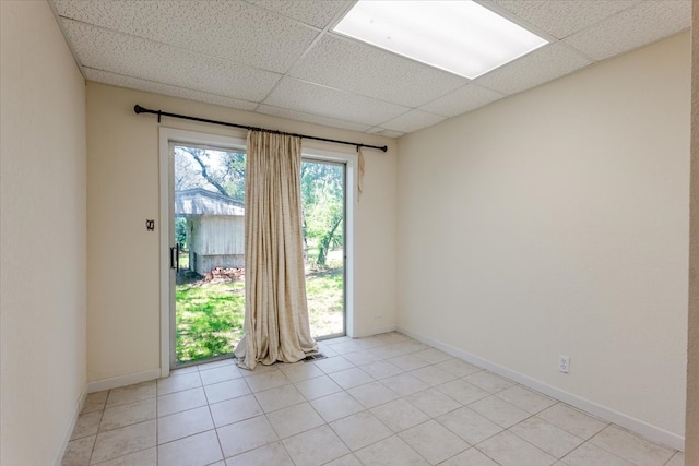 empty room with baseboards, a paneled ceiling, and light tile patterned flooring