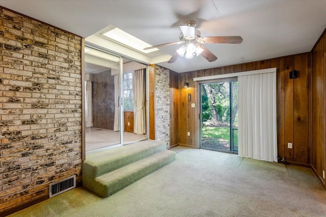 spare room with brick wall, wood walls, carpet, a ceiling fan, and visible vents