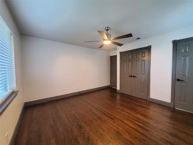 unfurnished bedroom featuring dark wood-style flooring, a ceiling fan, baseboards, visible vents, and a closet