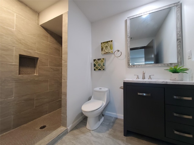 bathroom featuring vanity, baseboards, a tile shower, and toilet