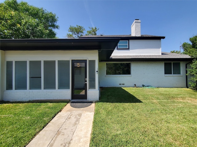 view of front of house with a shingled roof, a chimney, brick siding, and a front yard