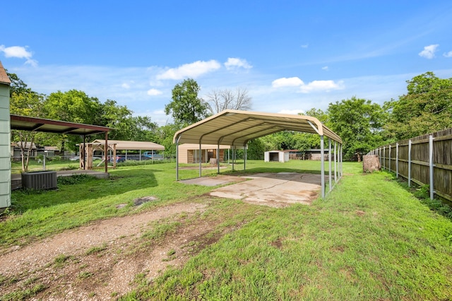 view of yard with a detached carport, fence, dirt driveway, central AC unit, and an outbuilding