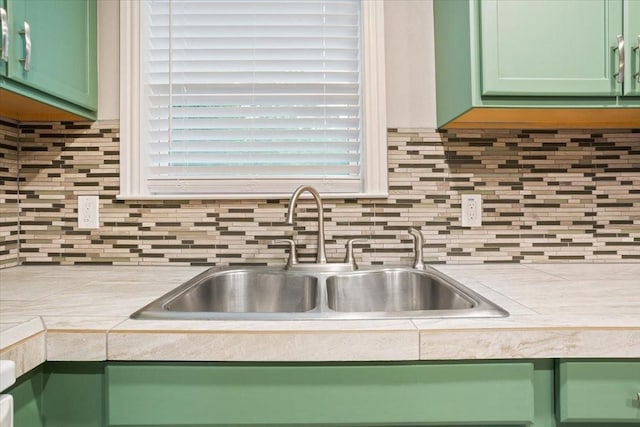 kitchen with light countertops, backsplash, green cabinetry, and a sink