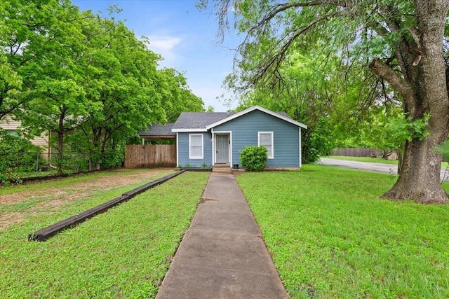 view of front of house featuring a front lawn, roof with shingles, and fence