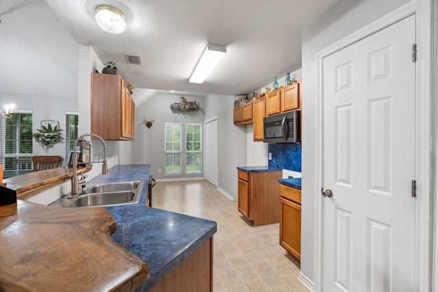 kitchen with visible vents, dark countertops, brown cabinets, a sink, and stainless steel microwave
