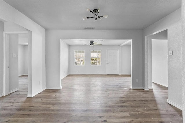 unfurnished living room with visible vents, baseboards, ceiling fan with notable chandelier, and wood finished floors