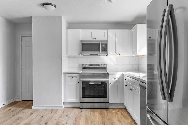 kitchen featuring appliances with stainless steel finishes, light countertops, light wood-style flooring, white cabinetry, and baseboards