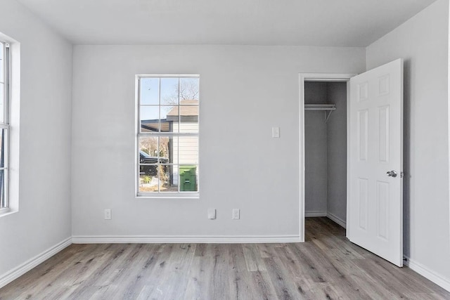 unfurnished bedroom with baseboards, a walk in closet, wood finished floors, and a closet