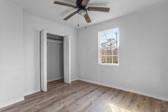 unfurnished bedroom featuring baseboards, ceiling fan, wood finished floors, and a closet